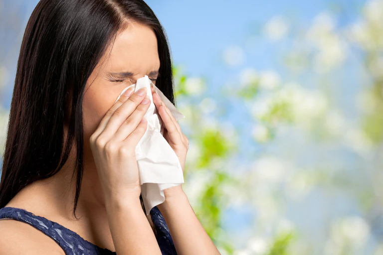 Woman blowing nose into tissue with summer wild flowers and blue sky in background