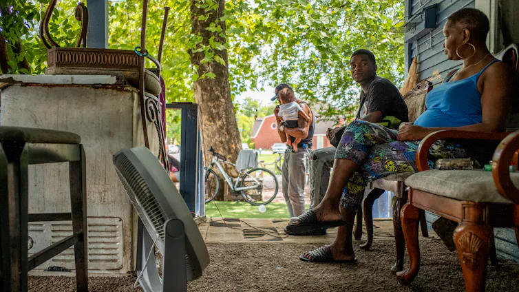 A family sits outside in the shade on a hot day
