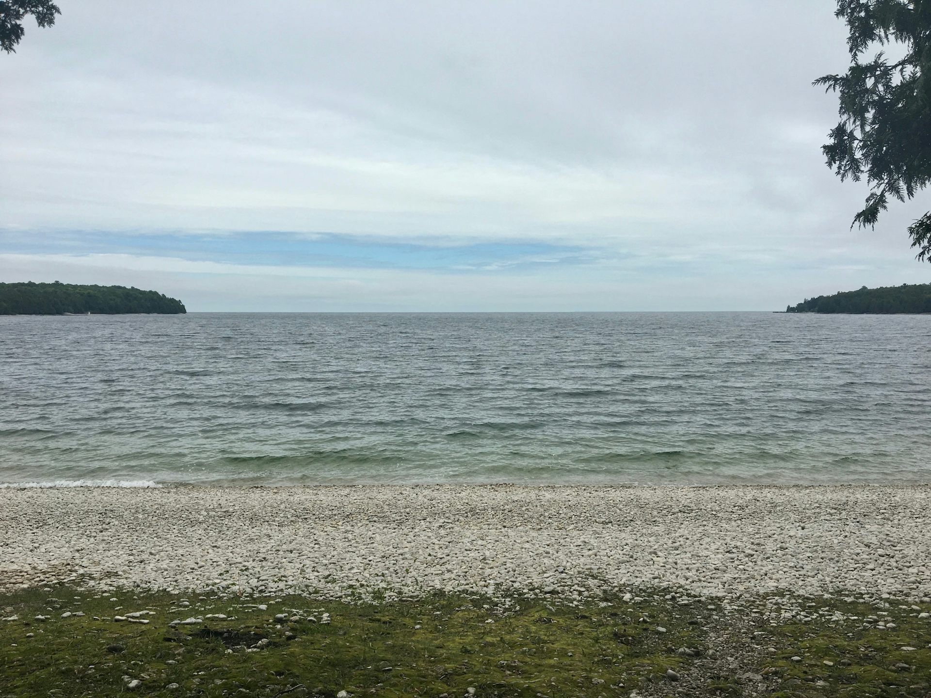 A view of a rocky beach looking out at a lake with tree-covered land in the distance.
