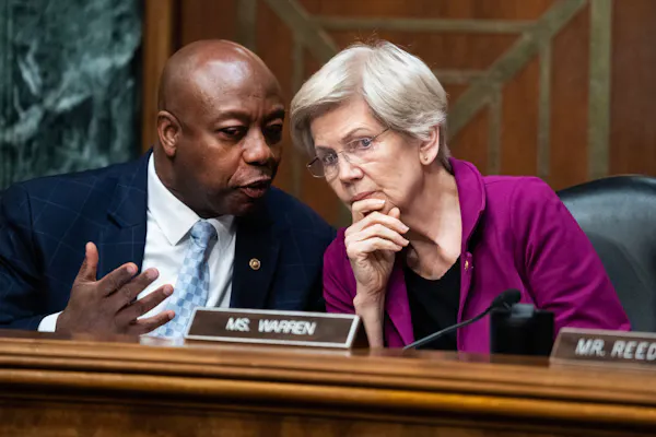 Middle-aged Black man wearing suit speaks to elderly woman seated to his right, who's leaning toward him and listening intently.