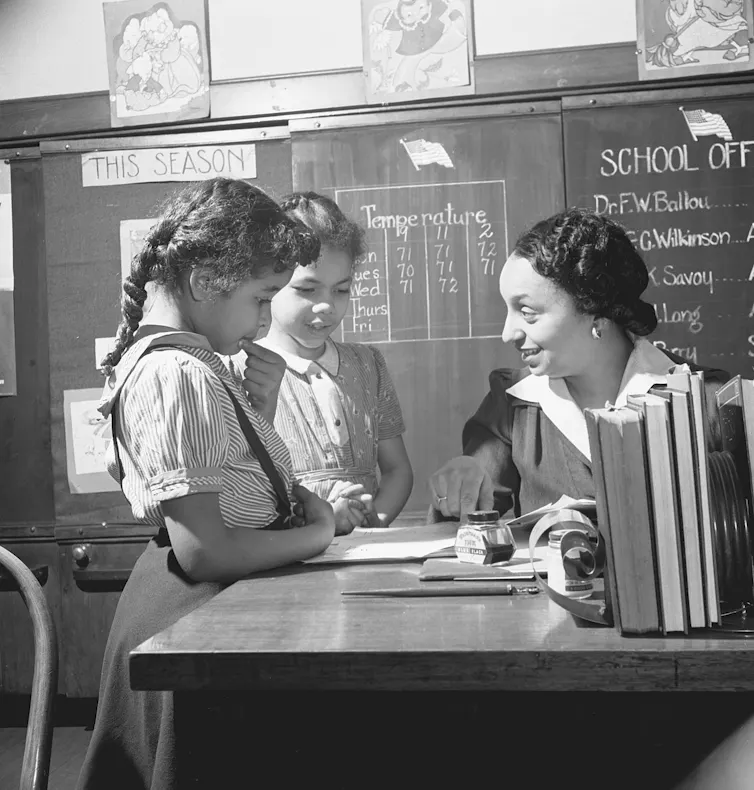 A woman sits at a table with two young girls in a black-and-white photo.
