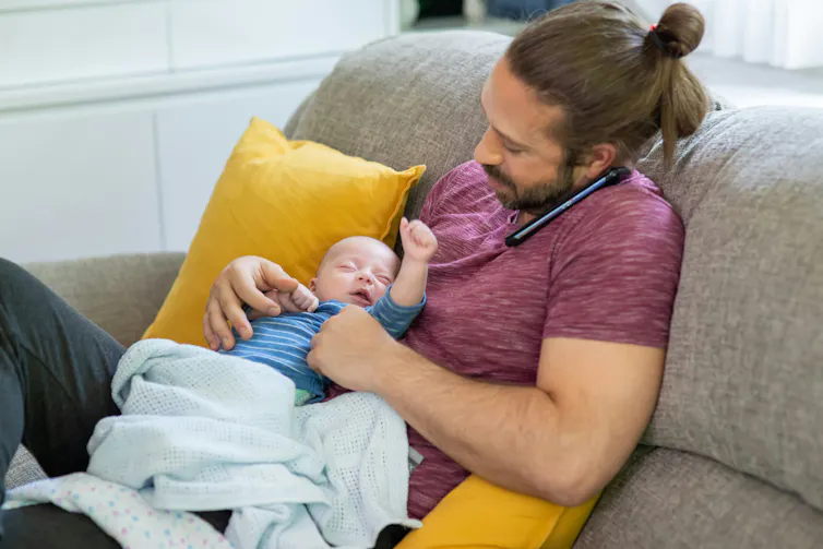 Cuando los hombres toman la baja por paternidad, sus carreras pueden beneficiarse, pero las mujeres no 1 Un hombre habla por teléfono mientras sostiene a un bebé en su regazo.
