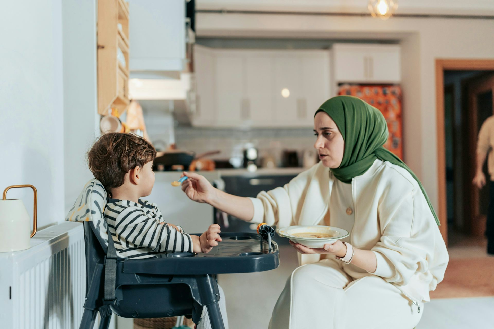 Una mujer con hijab alimenta a un niño en una silla alta