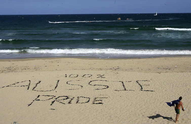 The words '100% Aussie Pride' are etched into the sand at a beach.