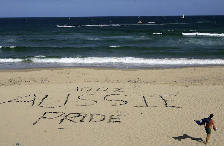 The words '100% Aussie Pride' are etched into the sand at a beach.