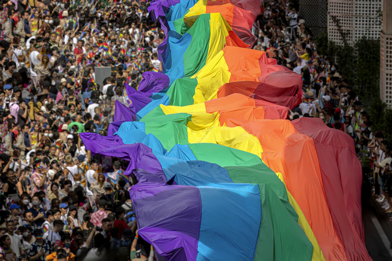 A crowd carries a giant Pride flag.
