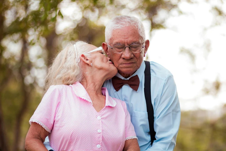 Elderly woman kissing cheek of elderly man, outside