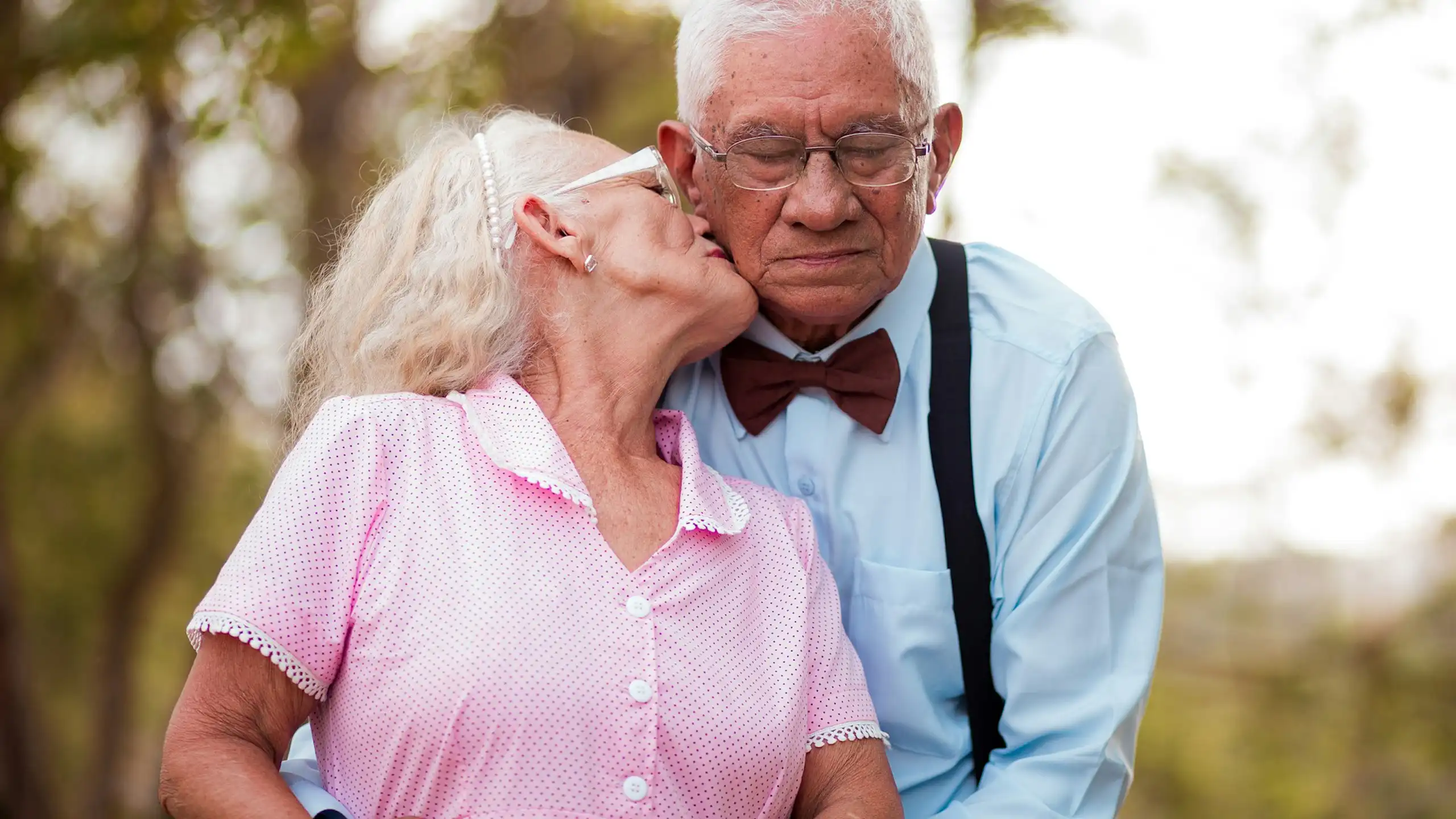Elderly woman kissing cheek of elderly man, outside