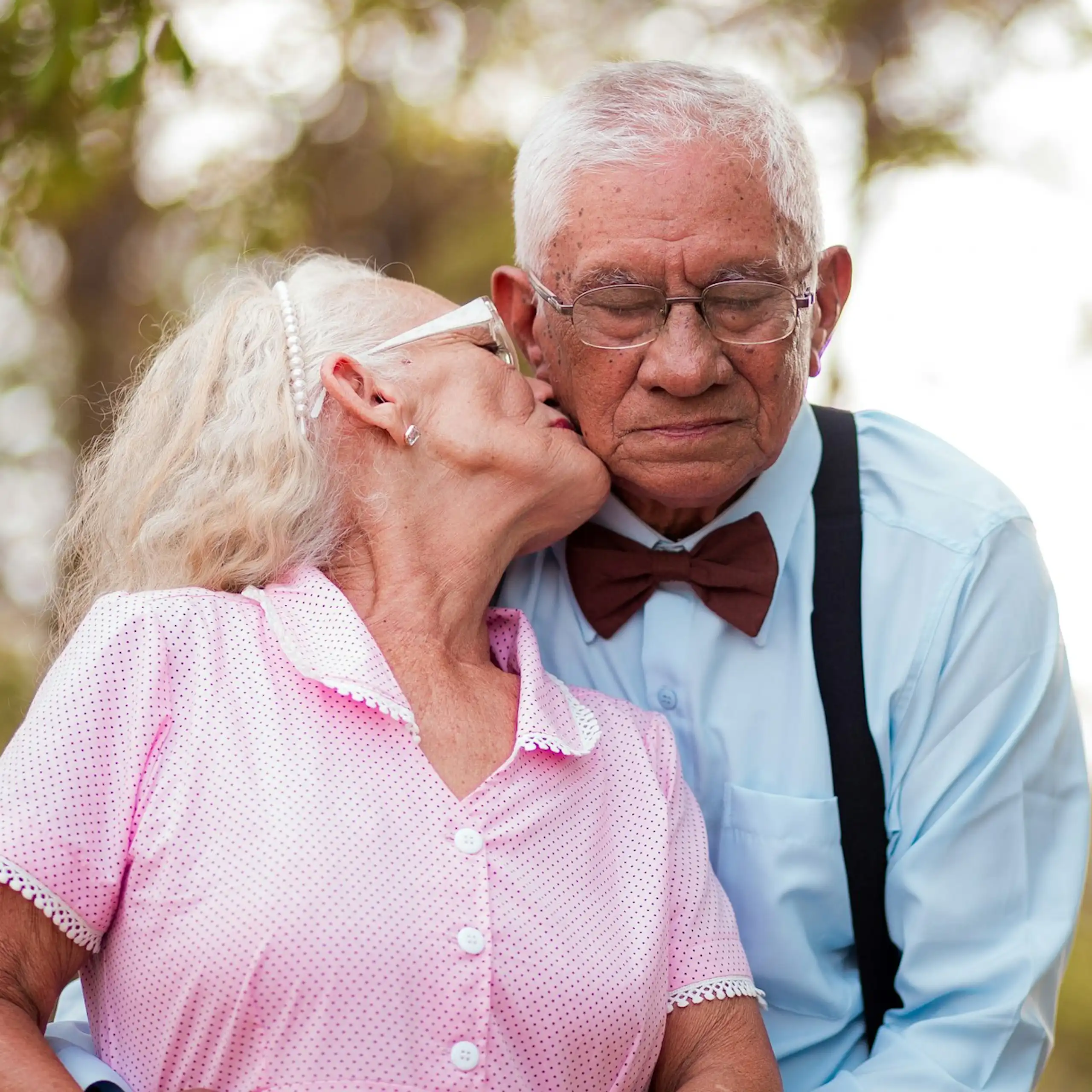 Elderly woman kissing cheek of elderly man, outside