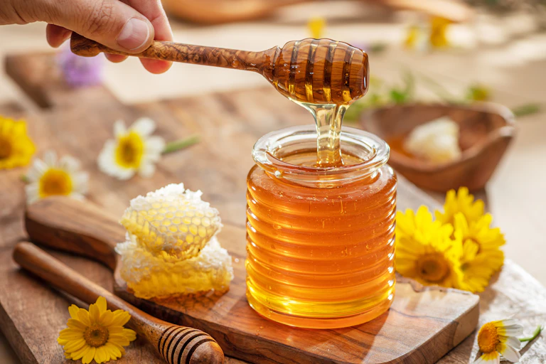 A hand picks up a spoonful of honey from a jar.