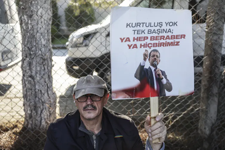 A supporter of jailed Istanbul mayor, Ekrem Imamoglu holds up a placard with a picture of Imamoglu and the phrase: 'There is no salvation alone, either all together or none of us':