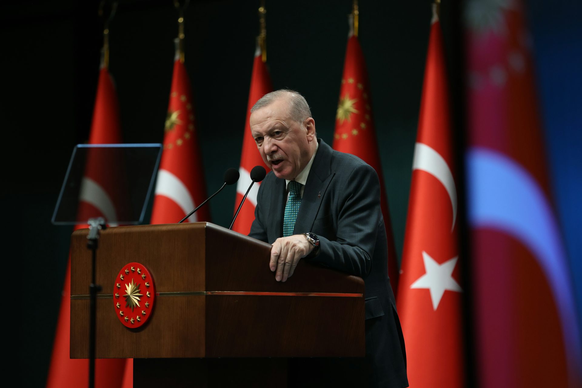 Turkey's president, Recep Tayyip Erdoğan, speaks on a podium surrounded by Turkish flags.