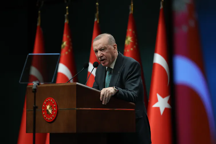 Turkey's president, Recep Tayyip Erdoğan, speaks on a podium surrounded by Turkish flags.