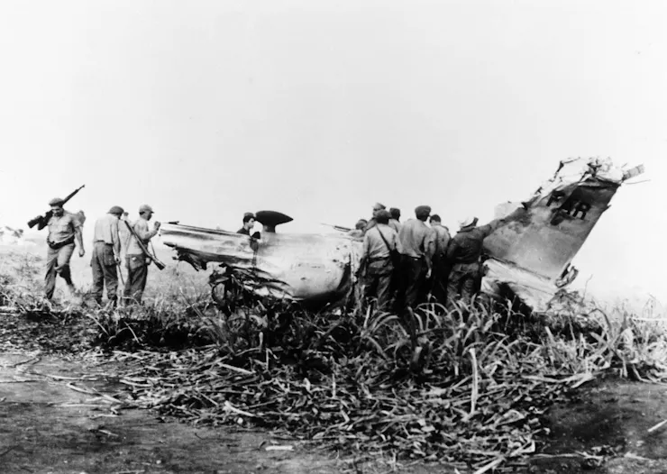 Several men in a black and white photo inspect the wreckage of a plane.