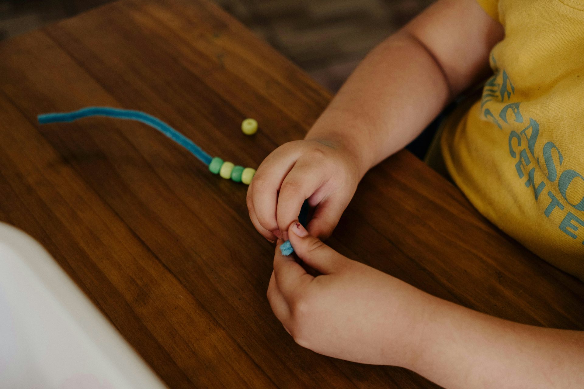 Los dedos gruesos de un niño en edad preescolar ensartan cuentas.