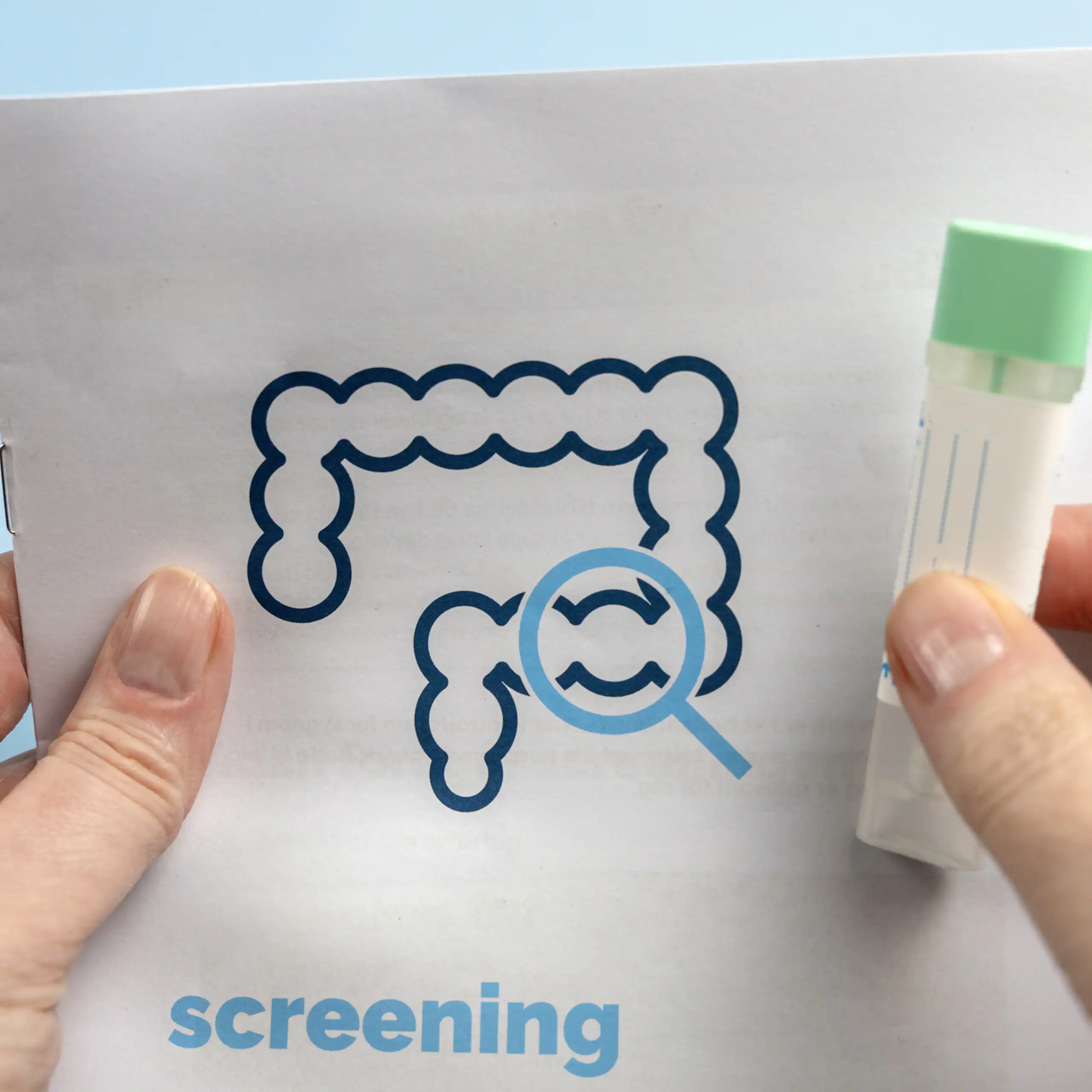 Close-up of hands holding a test tube and a packet with an icon of an intestine, a magnifying glass hovering over the colon and the word 'screening' printed on it