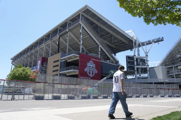 Una persona con jeans y camiseta blanca camina por un estadio al aire libre