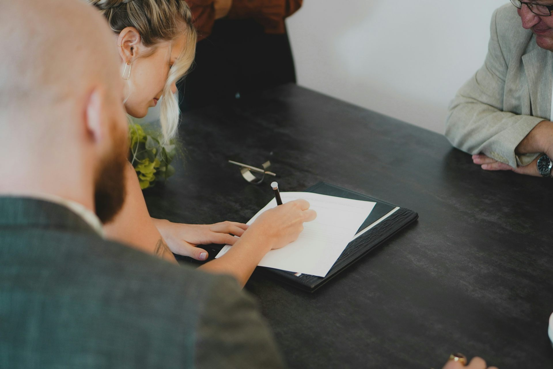 A woman signs a document while a man looks on