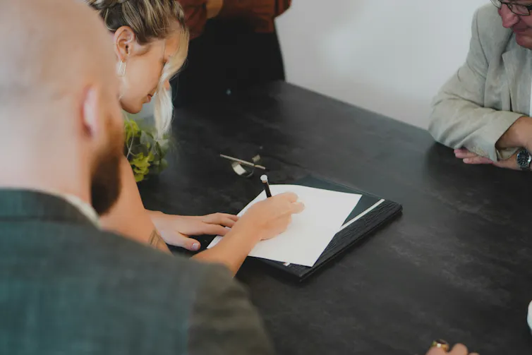 A woman signs a document while a man looks on