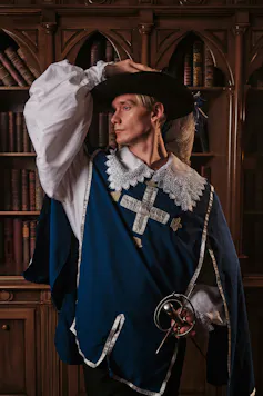 El período de la Regencia fue queer y trans. 'Bridgerton' apenas roza la superficie 1 Un hombre vestido con ropa de Regencia sostiene un sombrero en la cabeza con una mano y una espada con la otra.