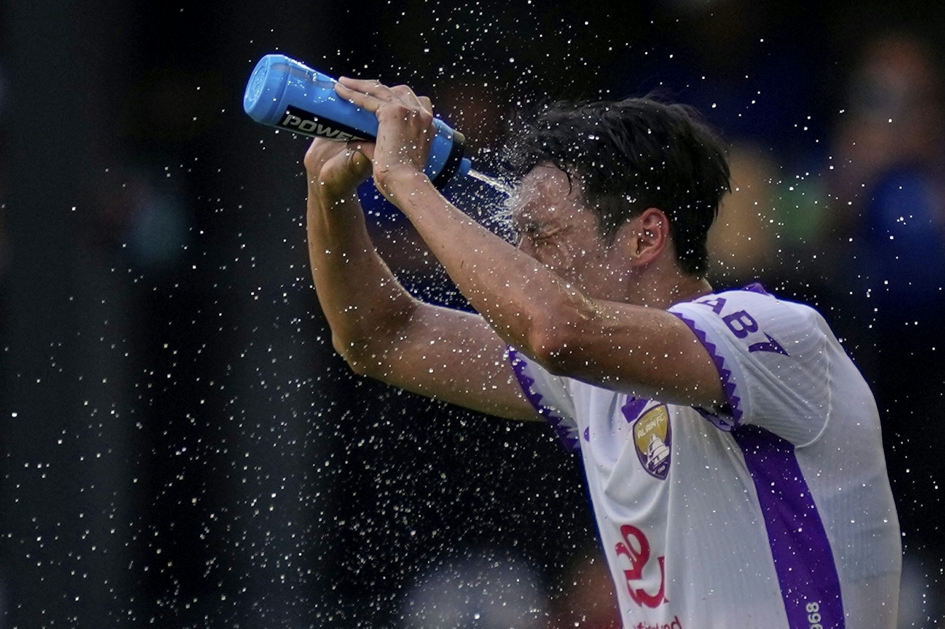 Un hombre con una camiseta de fútbol se salpica agua en la cabeza con una botella azul