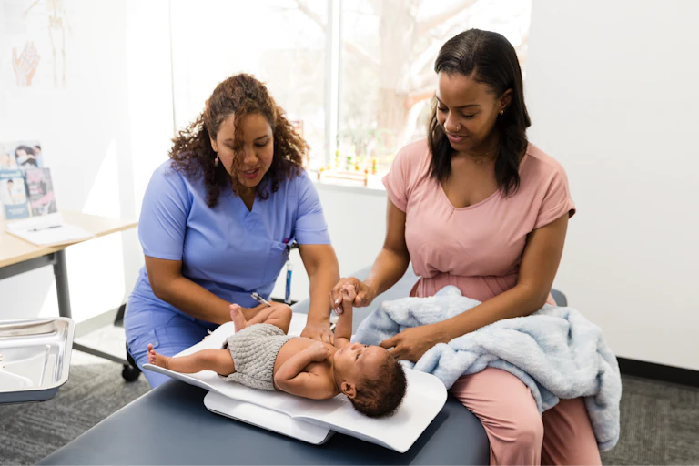 A nurse weighs a small baby while the mother watches on