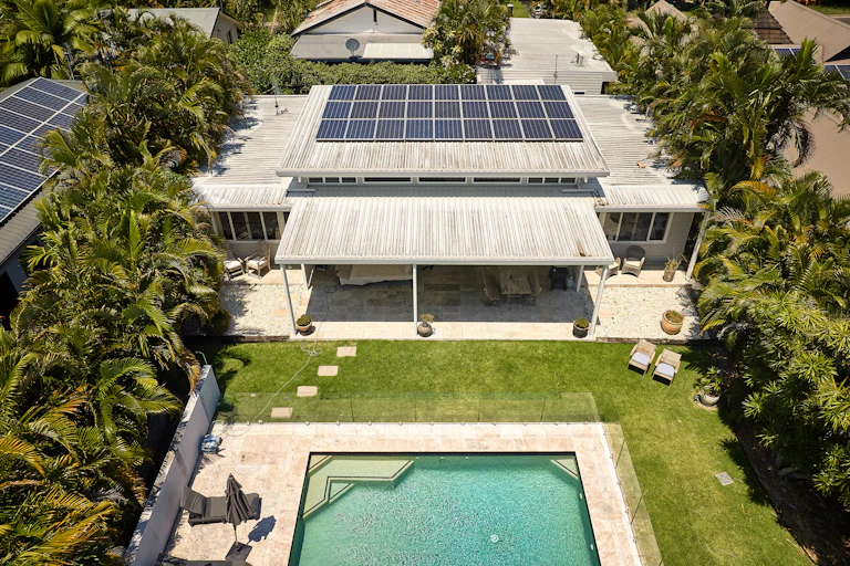 fancy house with a pool and solar on roof, surrounded by palm trees.