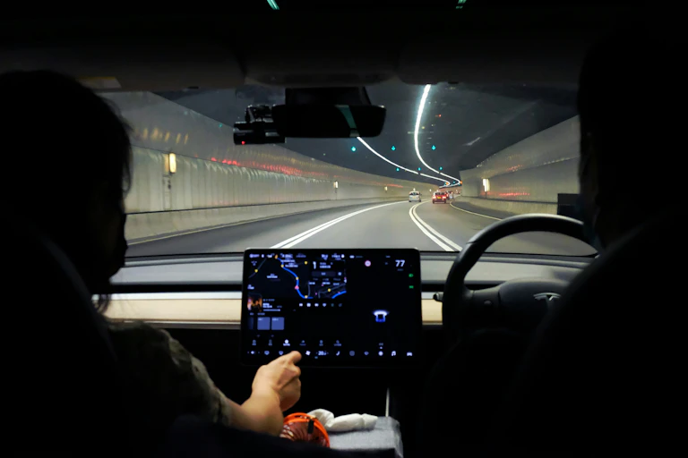 A view from the backseat of the car of the driver holding the steering wheel, moving through a tunnel.