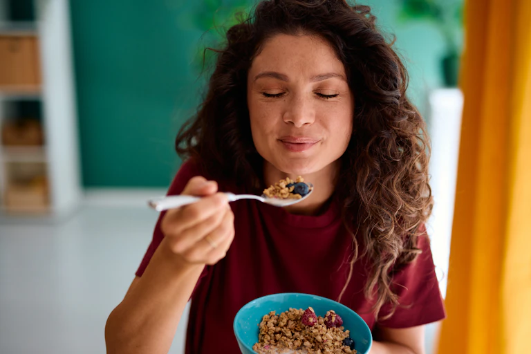 Young woman savoring a bowl of cereal while smiling.