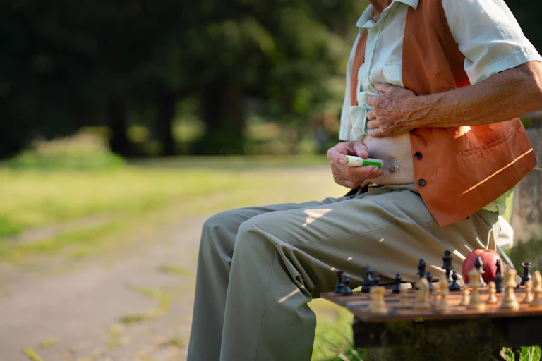 An elderly man sat on a park bench injects himself with insulin.