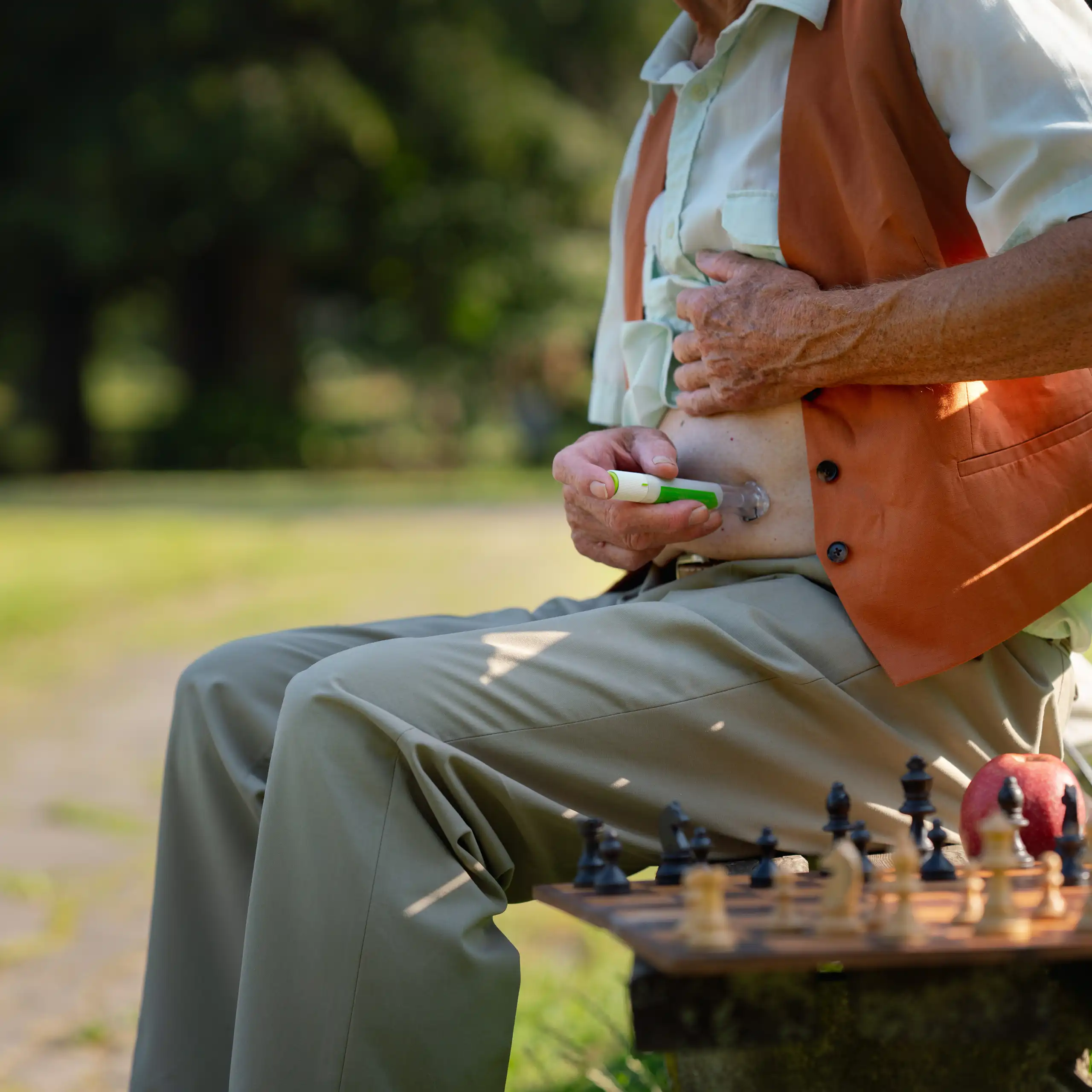 An elderly man sat on a park bench injects himself with insulin.
