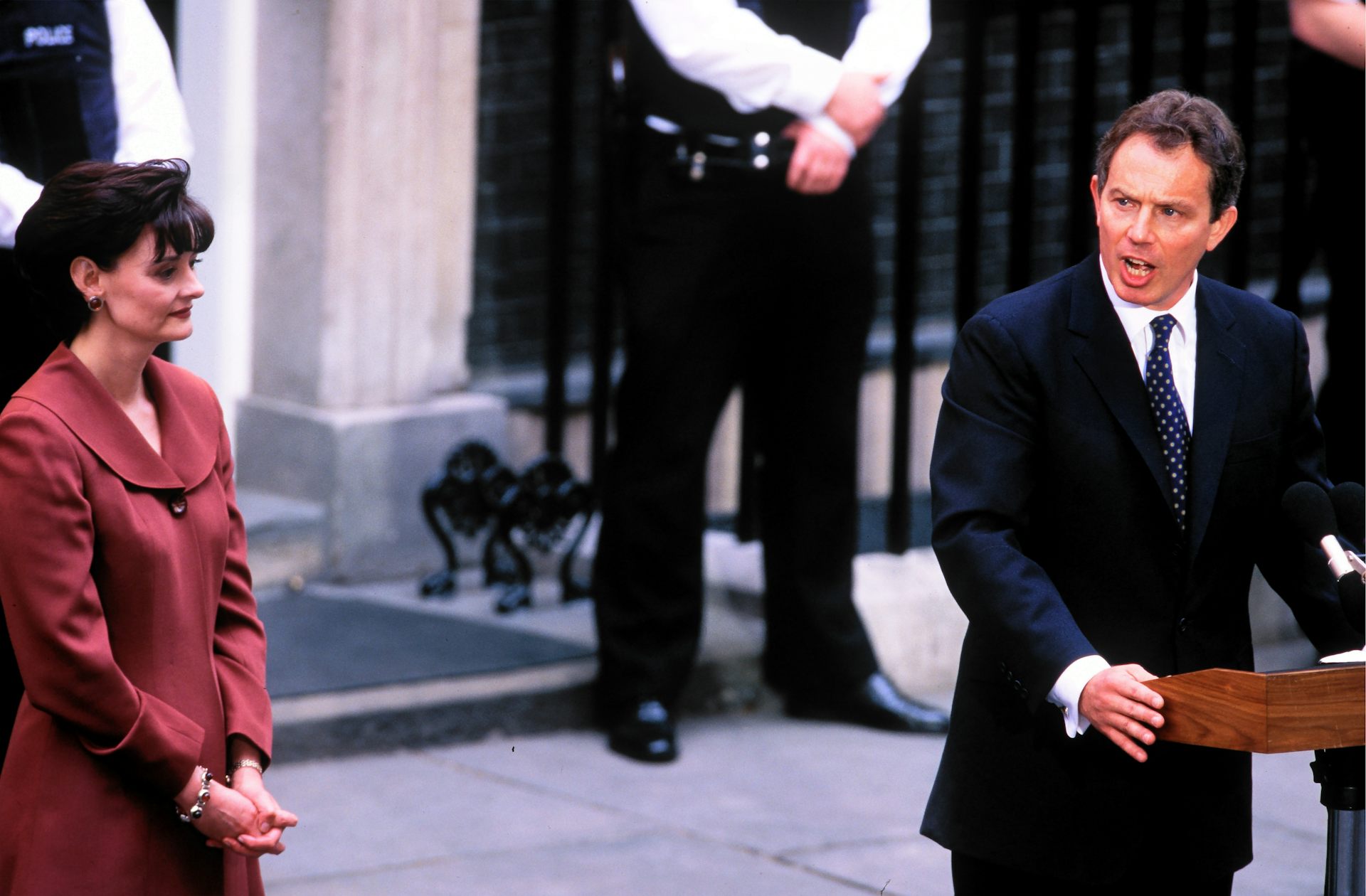 tony blair at a lectern outside number 10 after becoming prime minister in 1997 with wife cherie looking on.