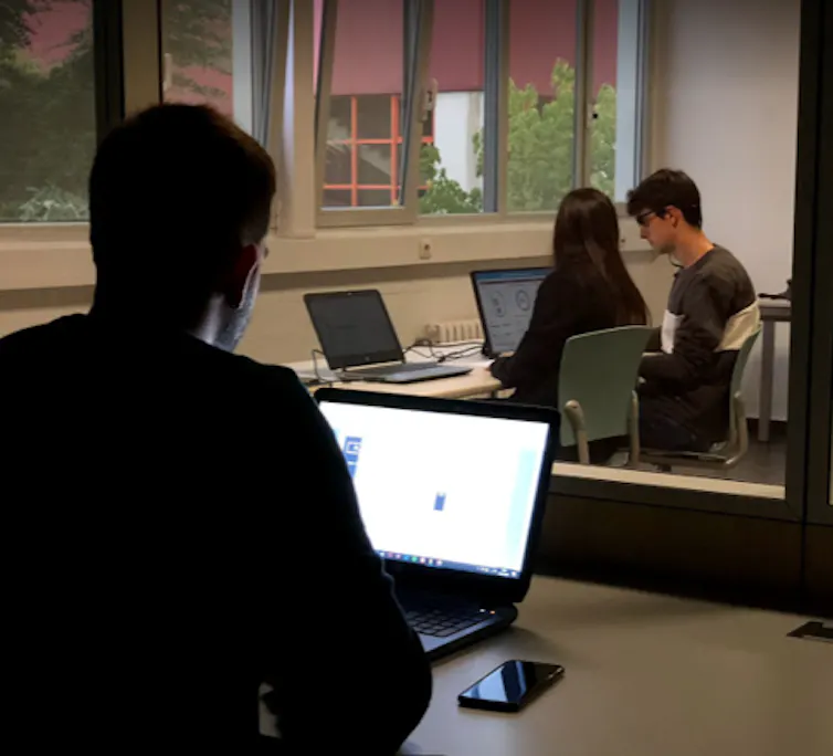 Escena de un test de usabilidad: un investigador observa desde una cámara Gesell mientras una persona participante realiza una tarea con el apoyo de una facilitadora.