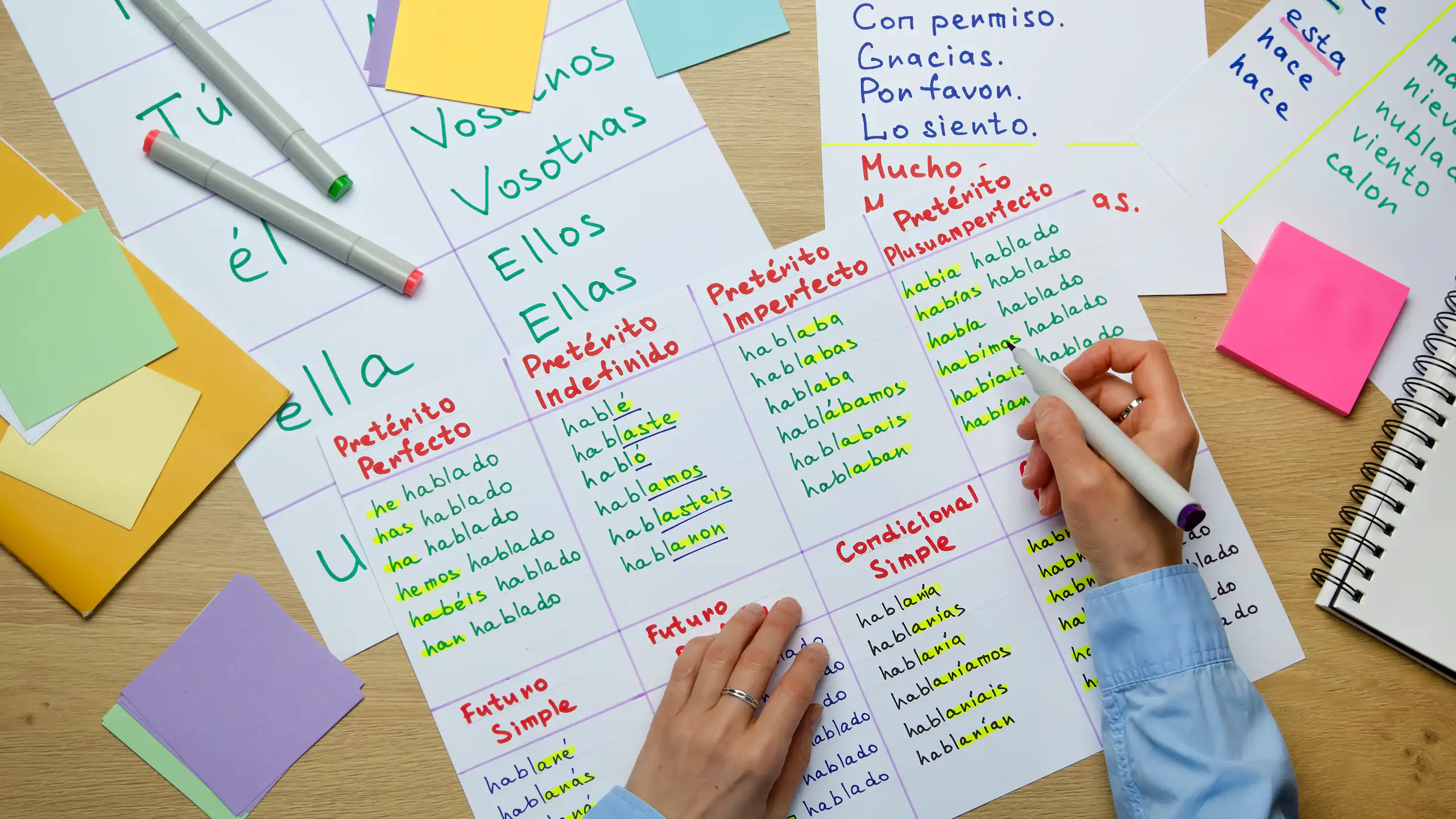 Vista cenital de unas manos infantiles escribiendo y hojas de ejercicios de escritura desperdigadas