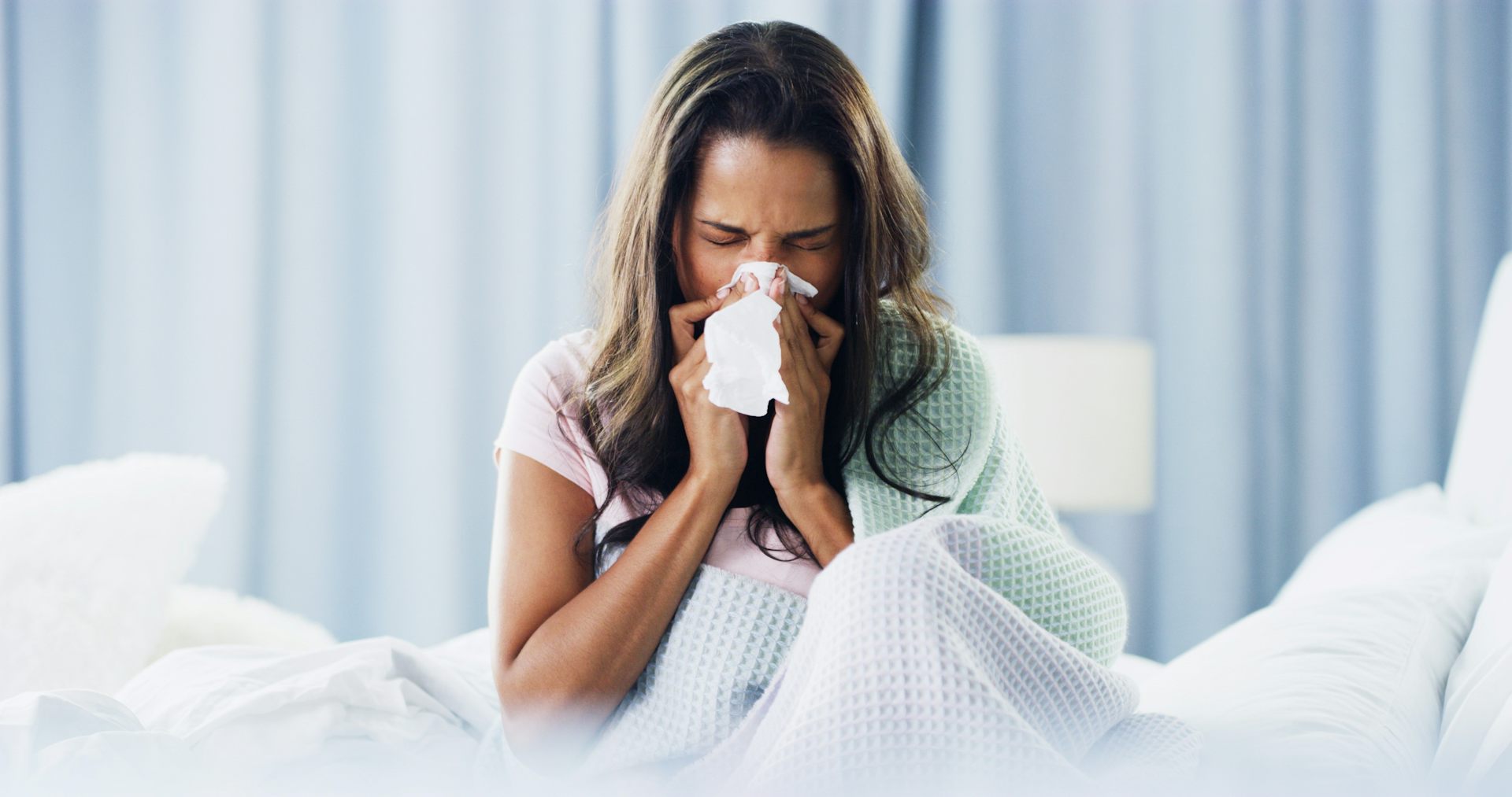 Woman blowing nose while in bed, kept awake by allergies