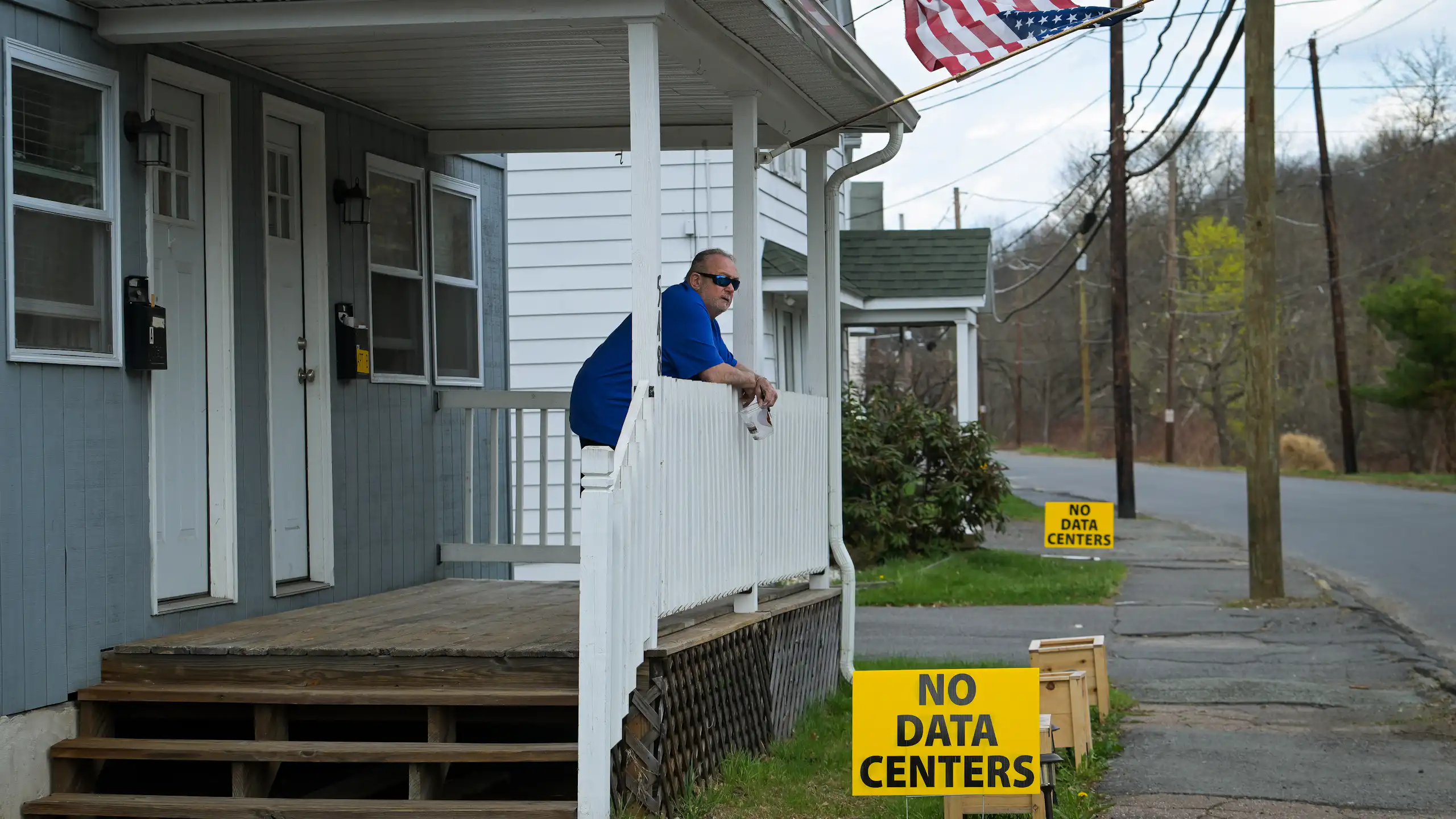 Man stands on front porch above yellow sign that says 'No Data Centers'