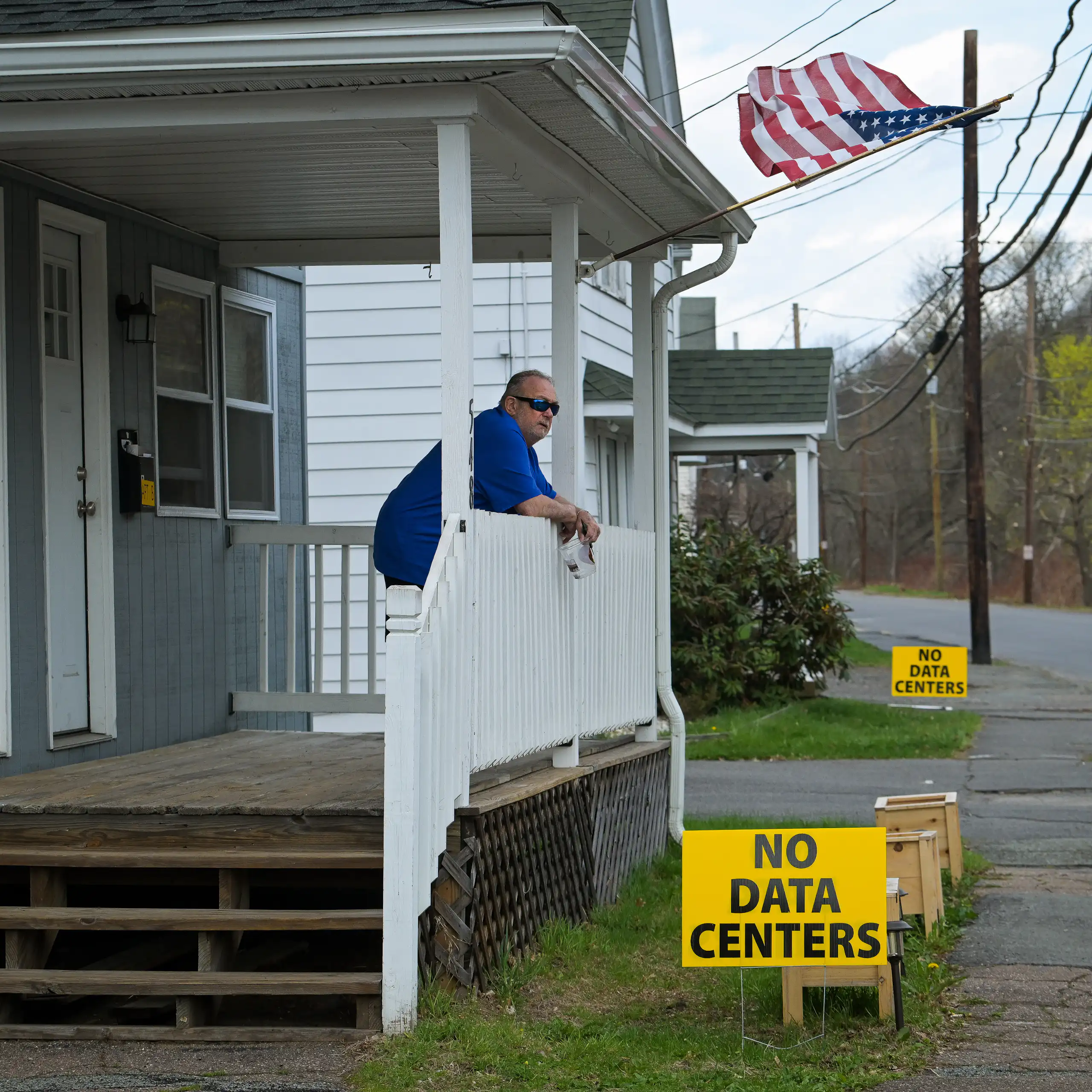 Man stands on front porch above yellow sign that says 'No Data Centers'