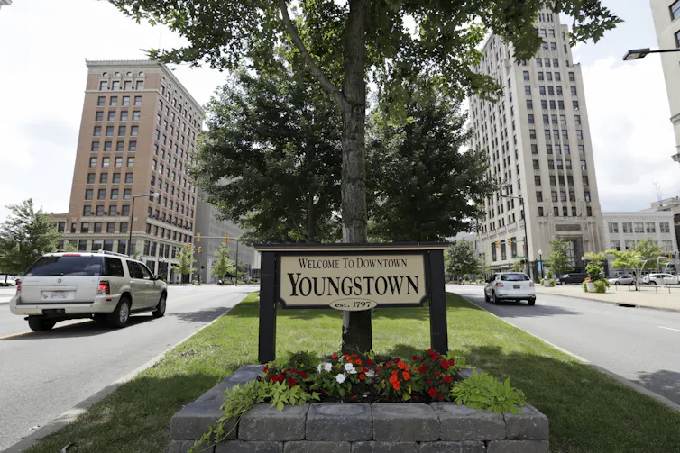 A sign in front of trees and flowers reads 'Welcome to Youngstown.'