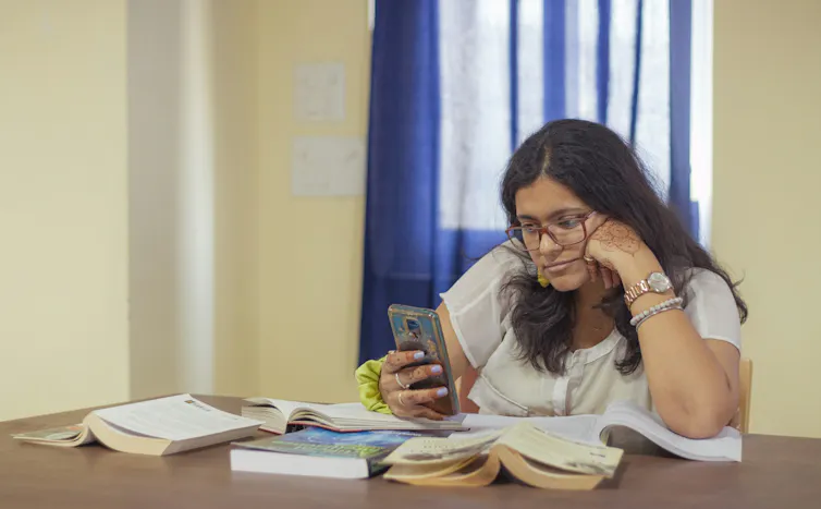 Las aplicaciones de enfoque fallan en las mentes neurodivergentes, según una nueva investigación 1 Una mujer con pelo largo y gafas mira fijamente su teléfono rodeada de libros sobre una mesa de estudio