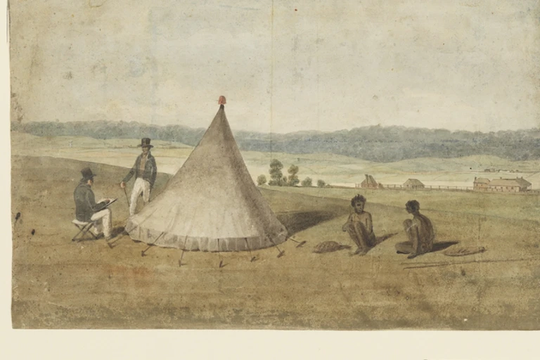 A large green field in front of a mountain range with a white tent and two Indigenous people