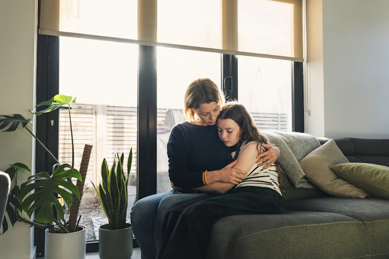 A woman hugs a young girl on a couch.