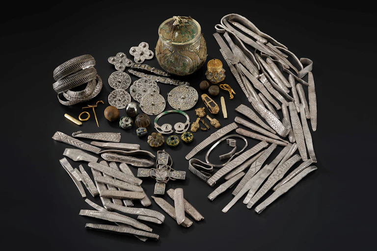 A hoard of (mainly silver) Viking treasure against a black backdrop.