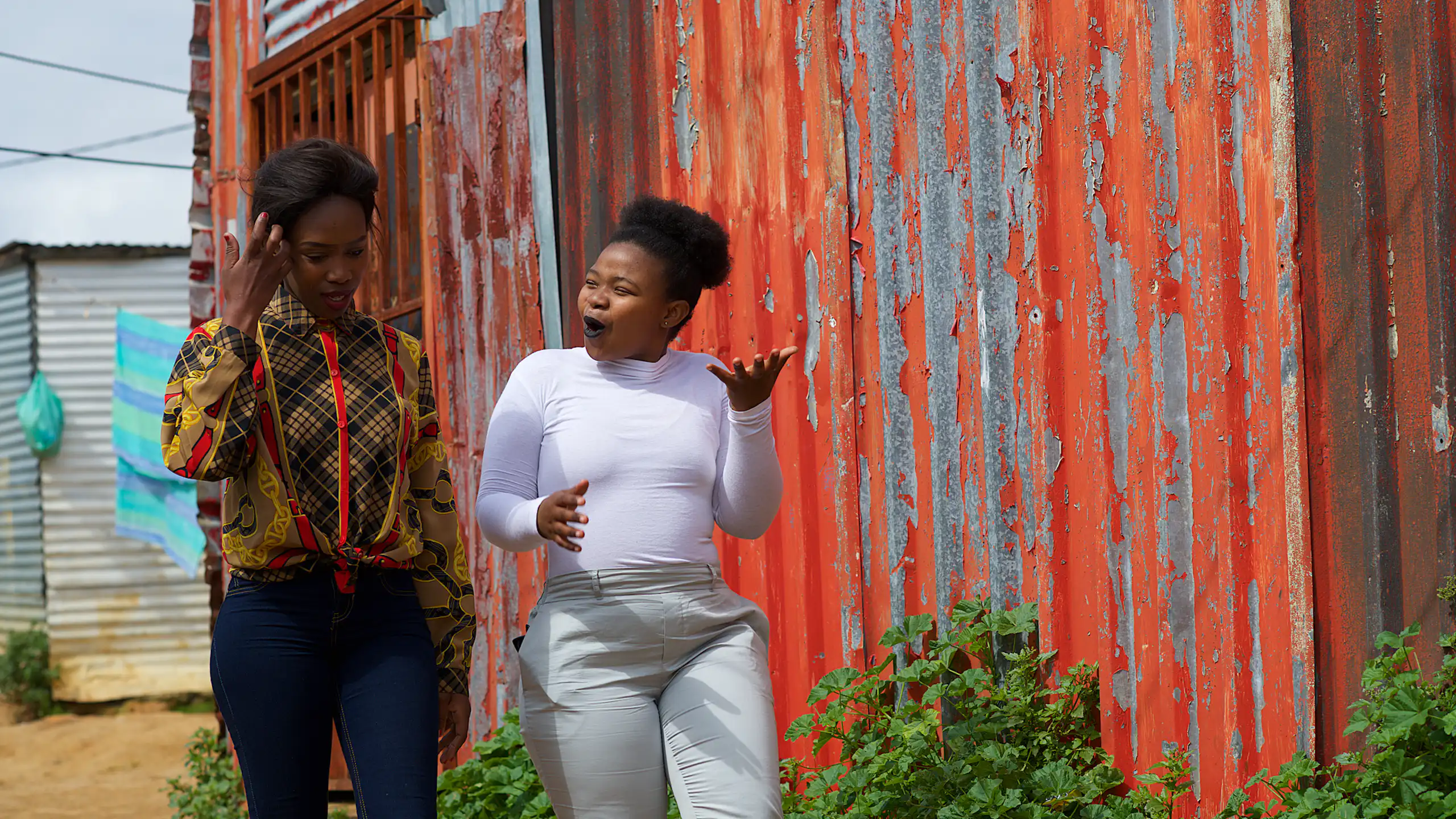 Two young women walking past a shack