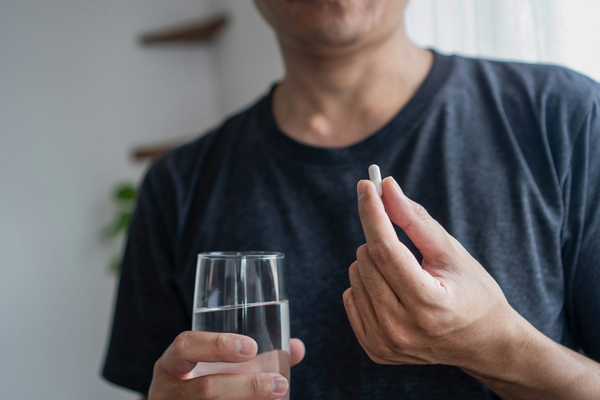 A man holding a probiotic supplement in one hand and a glass of water in the other.