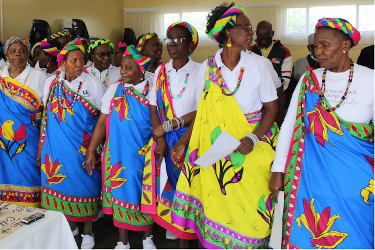 A group of women dressed in colourful traditional attire standing together and holding sheets of paper
