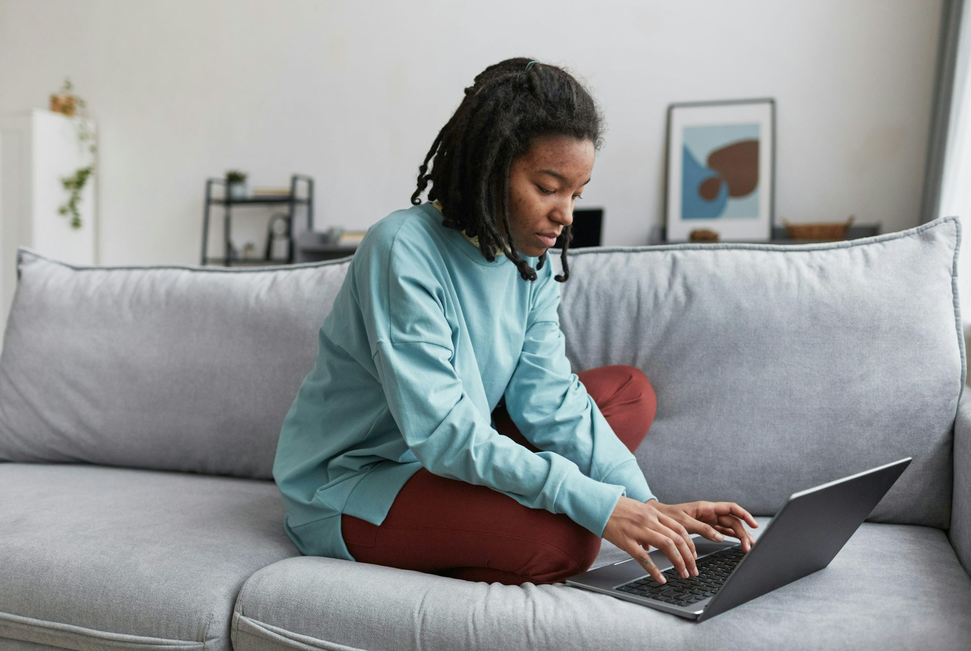 Une jeune femme sur son ordinateur est assise sur un canapé 