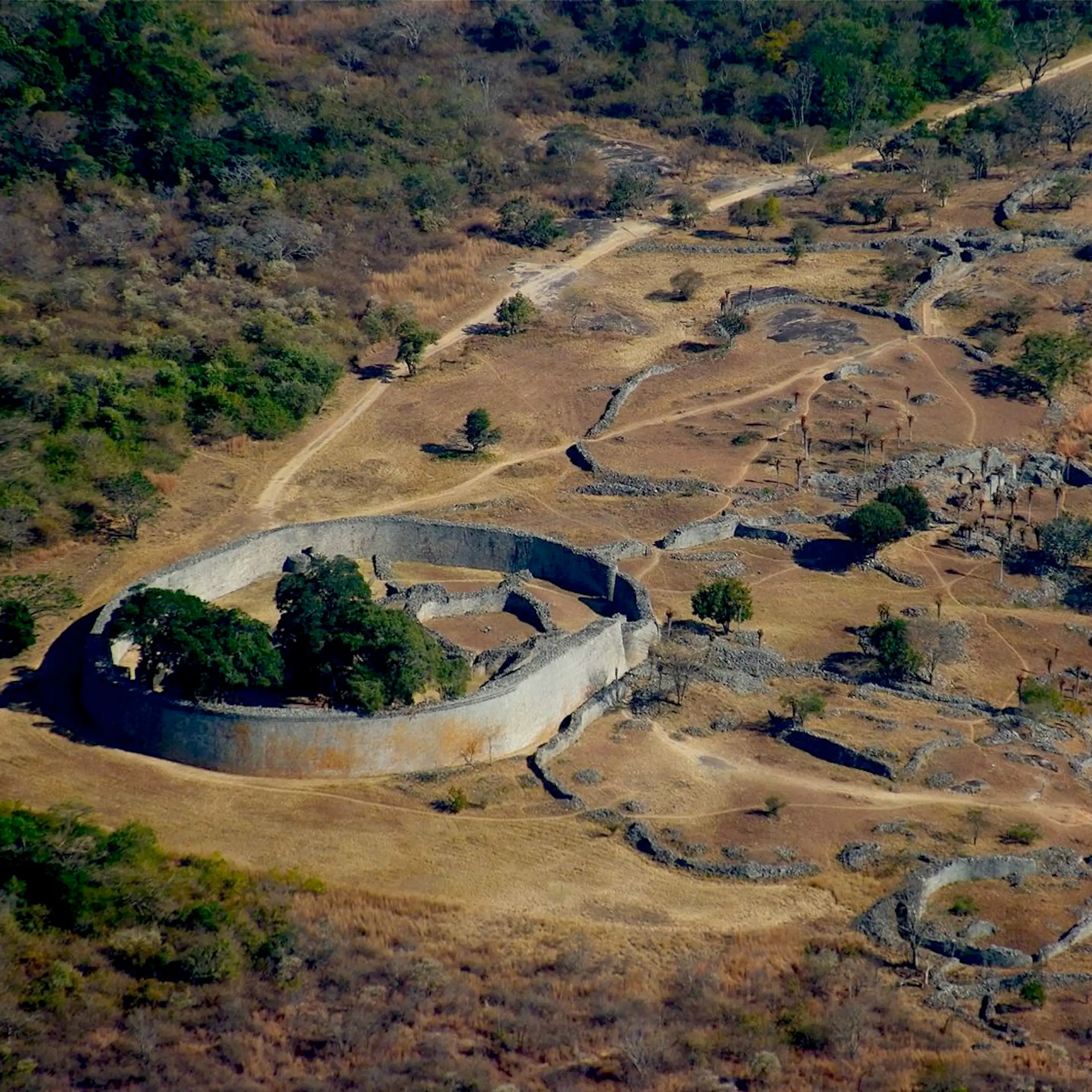 A large stone wall around a settlement in a valley leading to the remains of other settlements.