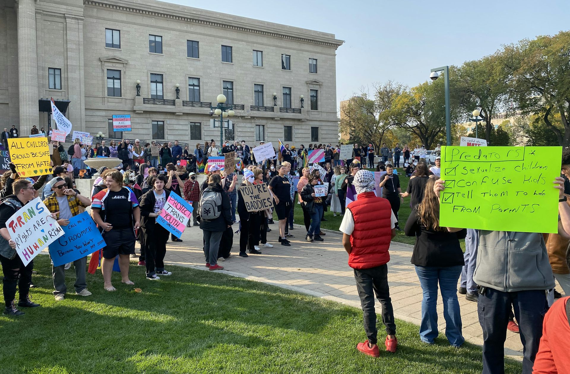 People holding placards in front of a legislative building with some signs saying 