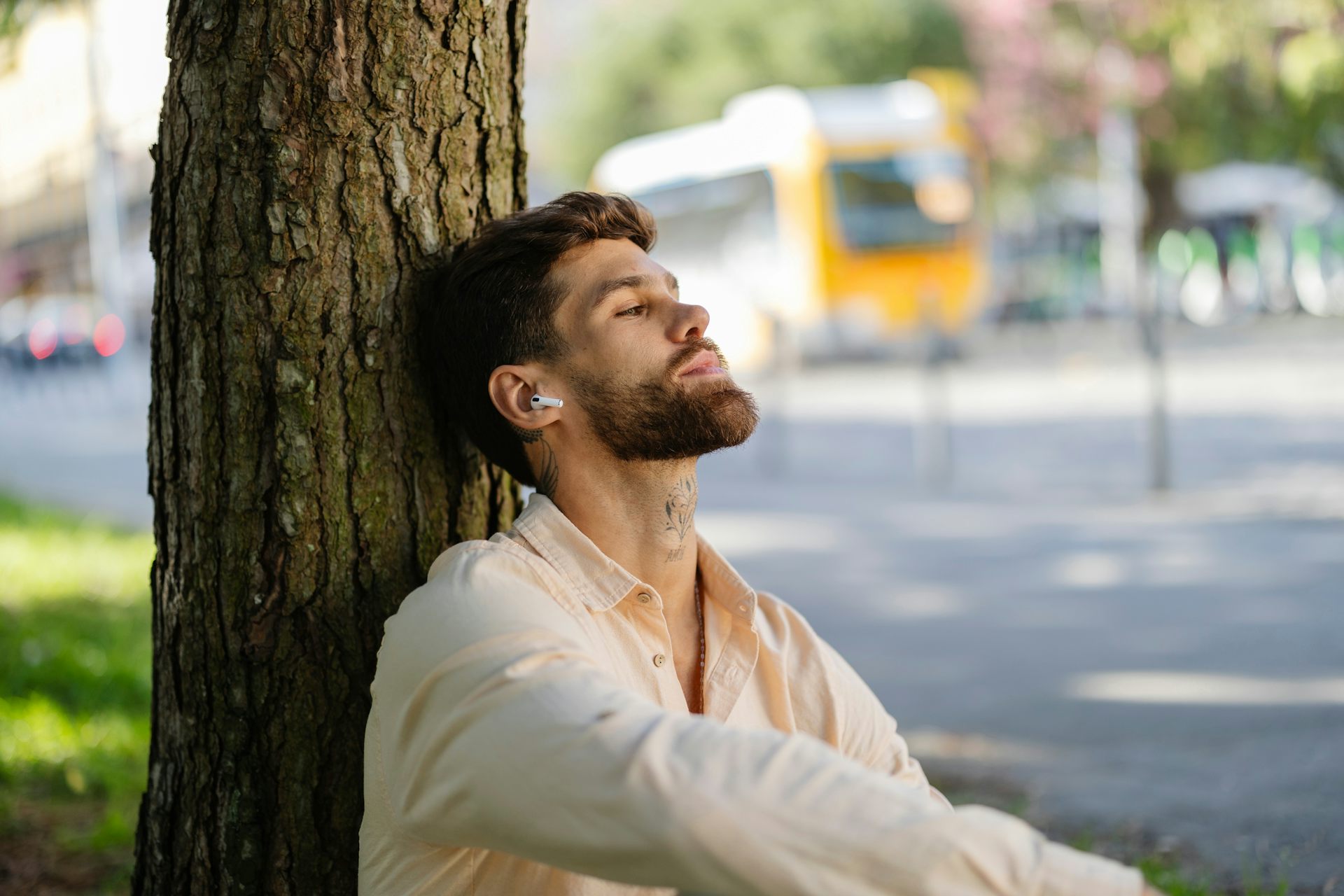 Young man leaning against tree with earphones in