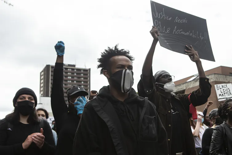 Un ajuste de cuentas inacabado con la violencia policial: los datos comunitarios muestran un racismo sistémico persistente 1 Un grupo de manifestantes con los puños en alto y carteles.